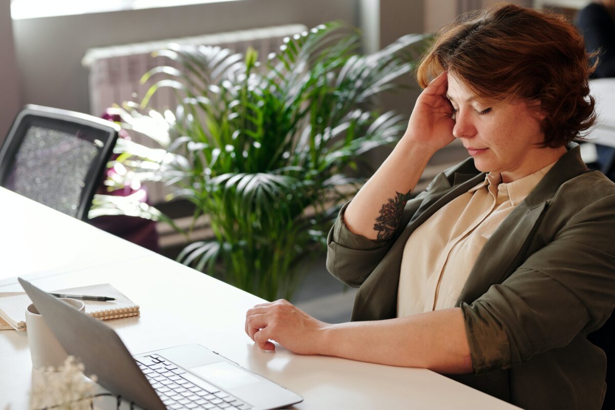 Image of a woman with her eyes closed and her hand to her head. She looks stressed.